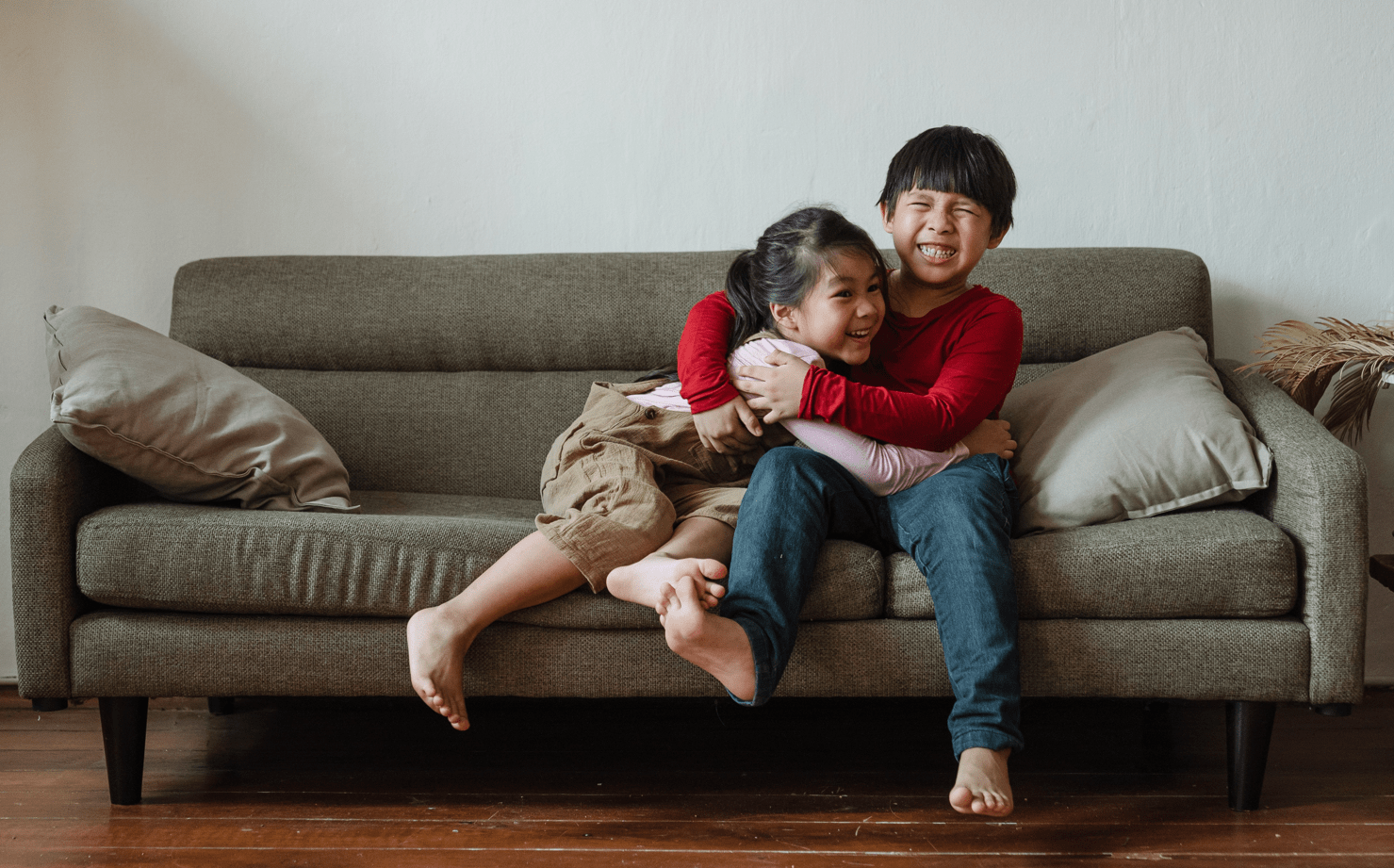 Two smiling kids playing on a brown couch