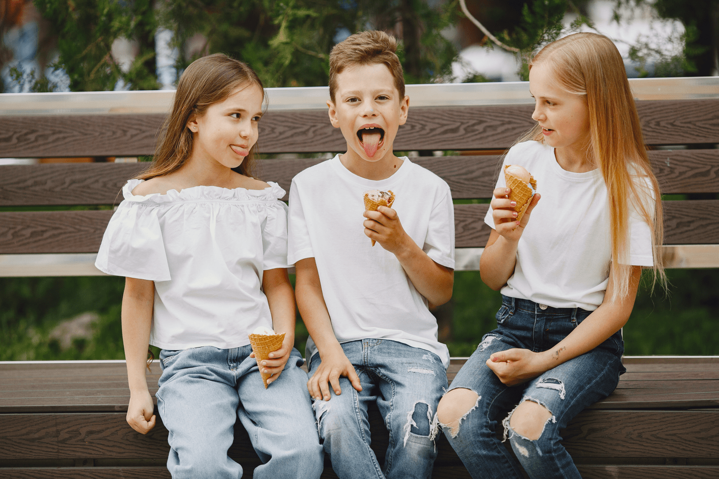 Kids eating ice cream on park bench while sticking out their tongue