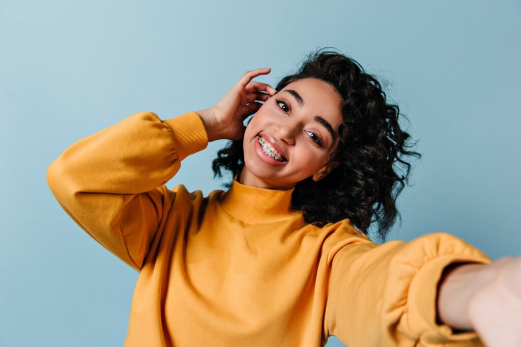 Woman with braces in orange shirt taking selfie