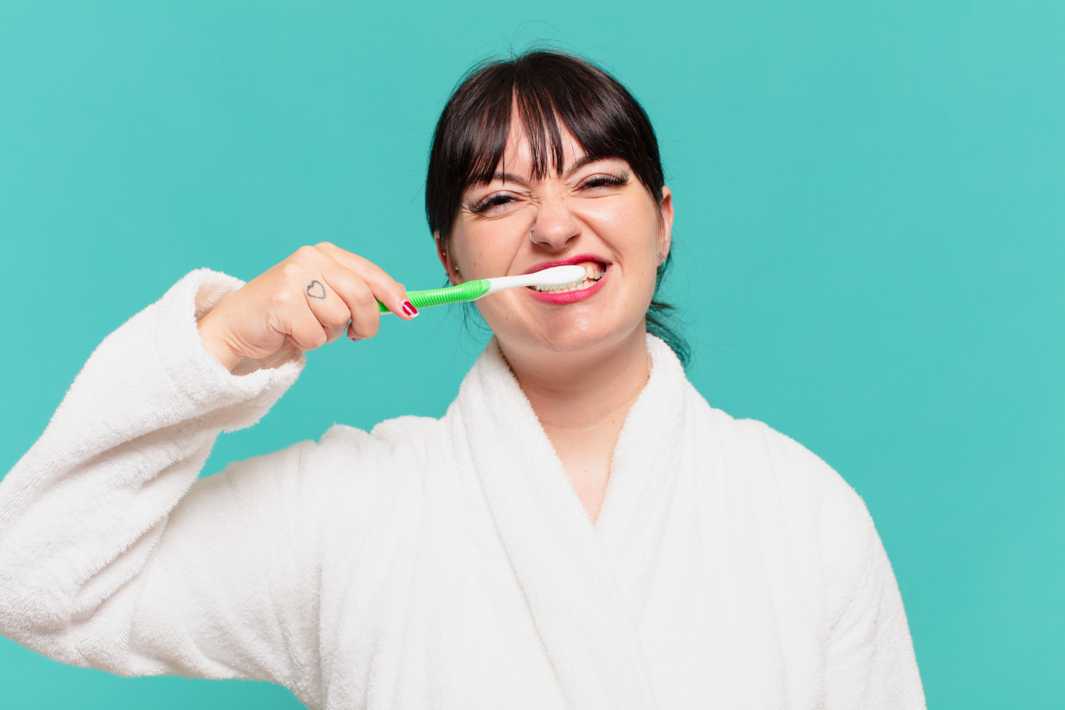 Woman brushing her teeth with a green toothbrush, promoting healthy dental habits.
