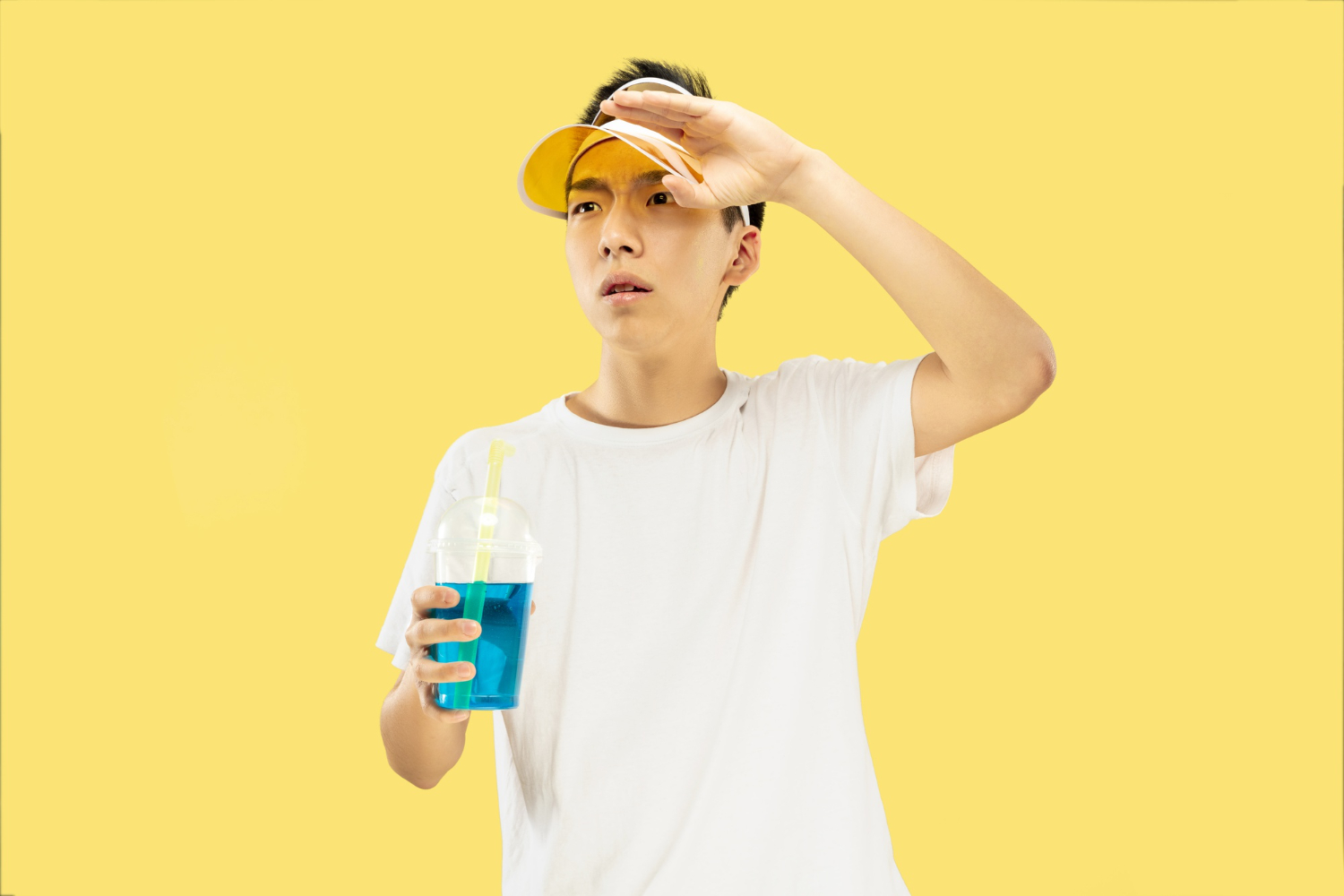 Teen boy wearing a visor and holding a blue drink while shielding his eyes from the sun.
