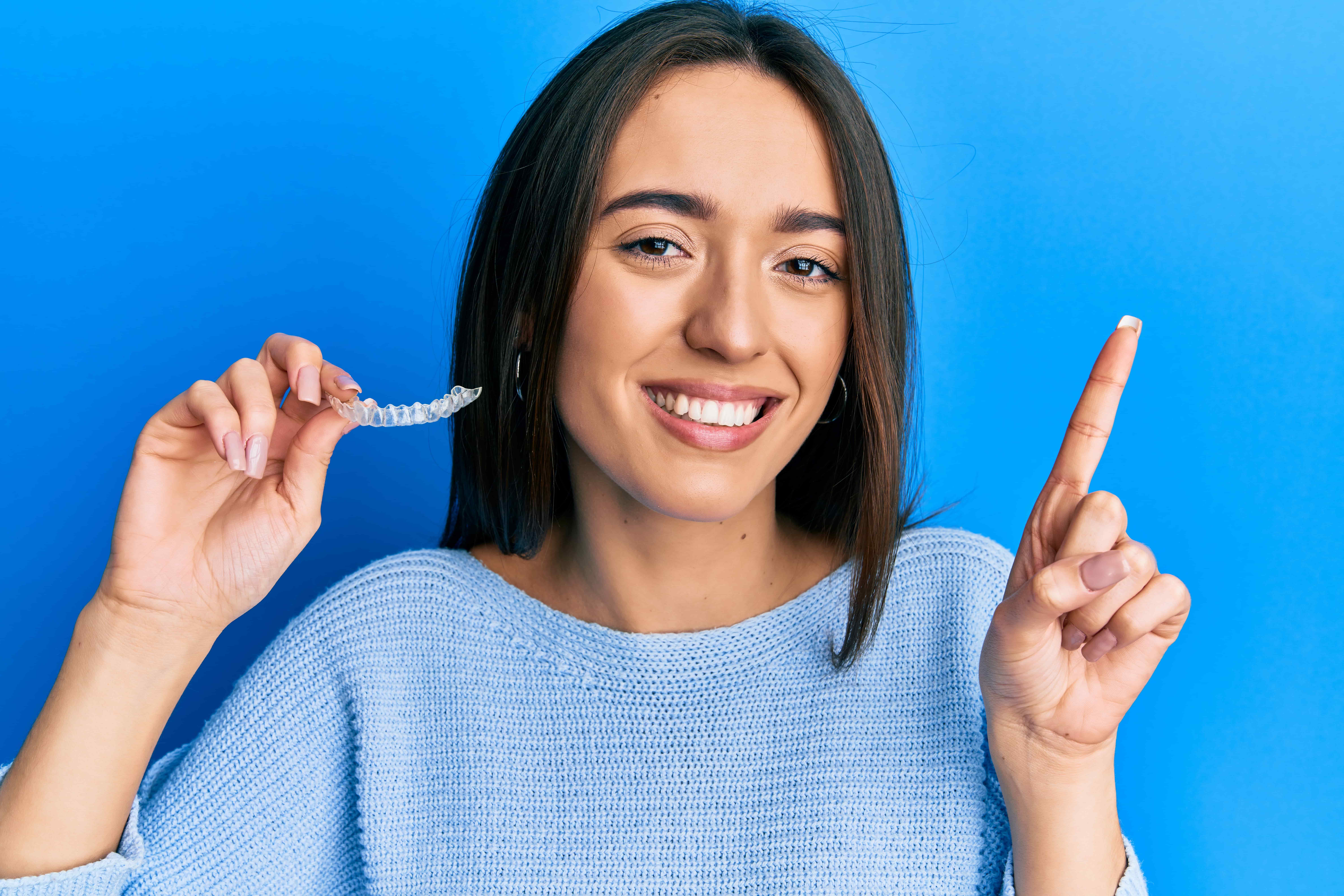 Young hispanic gir holding invisible align orthodontic smiling happy pointing with hand finger side